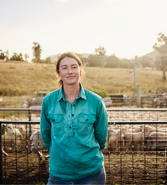 Lady in a blue shirt leaning against a farm gate with sheep in the background.