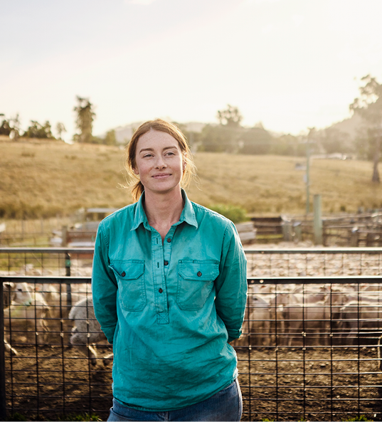 Lady smiling into the distance on a farm in front of sheep